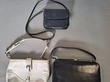 three purses are lined up on a table, one is black and one is white