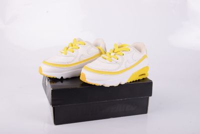 une paire de baskets blanches et jaunes posée sur une boîte noire