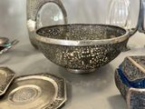 a silver bowl sitting on top of a table next to other silver dishes