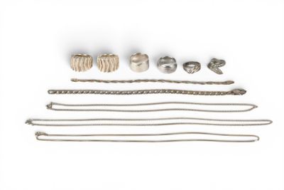 an assortment of silver jewelry on a white surface with a white background