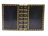 Deux livres noirs aux tranches dorées sont ouverts sur une surface blanche