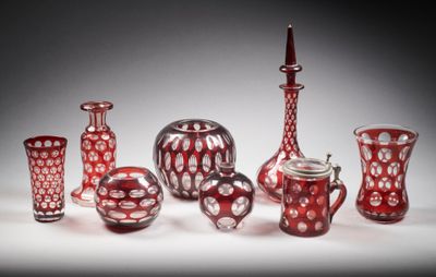 Plusieurs vases en verre rouge sont alignés sur une surface blanche