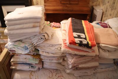 une pile de serviettes pliées sur un lit, dans une chambre où se trouve une commode