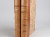 two brown books sitting on top of each other on a white surface