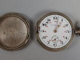 une montre de poche en argent posée sur une table à côté d'une horloge