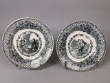 two blue and white plates with figures on them sitting on a table