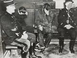 three men sitting on a bench in a room with a man in a gas mask on his face