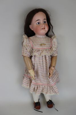 une vieille poupée vêtue d'une robe rose et de chaussures marron, posée sur une surface blanche