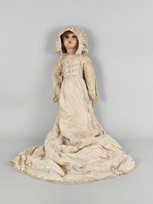 une poupée ancienne représentant une femme vêtue d'une robe blanche et d'un bonnet