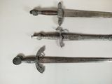 three old swords are displayed on a white surface