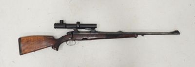 Un vieux fusil repose sur une surface blanche ; il est équipé d'une lunette de visée.