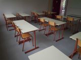 tables and chairs in a classroom with a projector screen in the background