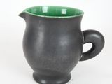 a black cup with a green handle on a white surface