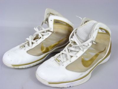 une paire de baskets de basket-ball Nike blanches et dorées posées sur une surface blanche