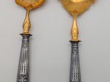 two silver and gold serving utensils on a white surface
