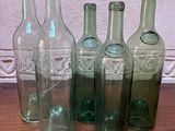 Six bouteilles en verre vert sont alignées sur une table en bois.