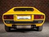 the rear end of a yellow sports car parked in front of a brick wall