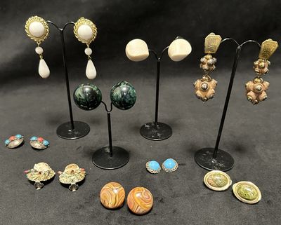 several pairs of earrings and brooches are displayed on a stand