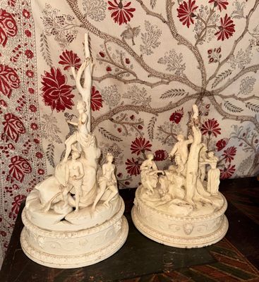 deux statues posées sur une table, avec en arrière-plan un papier peint rouge et blanc