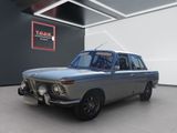 Une vieille voiture est garée dans une pièce où est accrochée une affiche au mur.