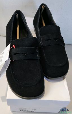 mocassins en daim noir pour homme, avec une boîte blanche posée sur un fond blanc