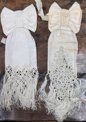 two pairs of white gloves with bows and fringes on a wooden surface