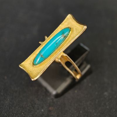 une image représentant une bague en or sertie d'une pierre turquoise sur un fond noir
