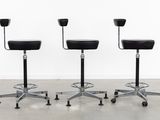 three black stools sitting on top of each other in front of a white wall
