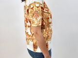 the woman is wearing a white shirt with a gold pattern on it