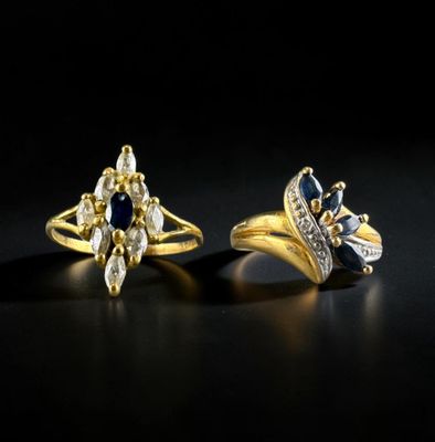 two gold rings with diamonds and sapphires on a black background