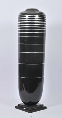 a large black vase sitting on a stand on a white surface