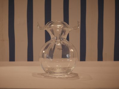 a glass vase sitting on a table with a striped wall behind it