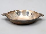 une assiette en argent antique avec une poignée sur une surface blanche