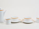 un service à thé blanc aux bords orange posé sur une table blanche