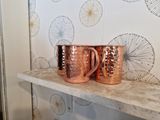 two copper mugs sitting on a shelf in a room