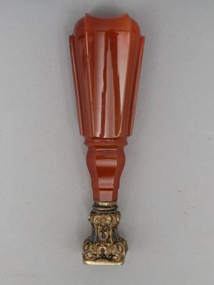 un vase en verre orange avec un socle doré posé sur une surface blanche