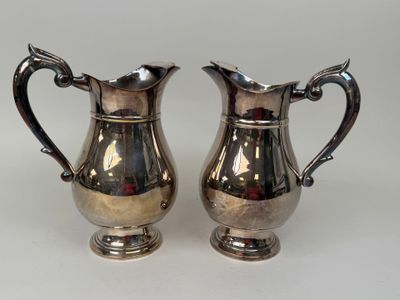 pair of silver plated pitchers with handles on a white surface