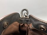 someone is holding a brown purse with a metal hook in it