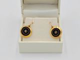 une paire de boucles d'oreilles noires et dorées dans un écrin sur fond blanc