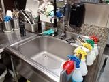 évier en acier inoxydable dans une cuisine professionnelle où se trouvent de nombreux produits d'entretien