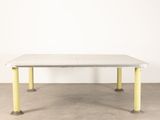 a white table with yellow legs sitting on a cement floor