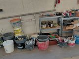 Plusieurs seaux de peinture sont alignés sur le sol d'un garage