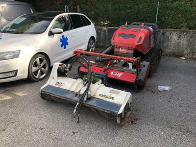 deux tondeuses à gazon sur un parking, à côté d'une voiture