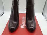 des bottines en cuir noir posées sur une boîte rouge, elle-même posée sur une surface blanche