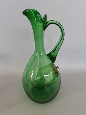 un pichet en verre vert muni d'une anse, posé sur une surface blanche