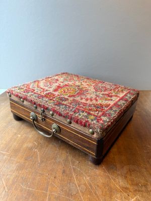 a small wooden box on a wooden table with a red and white rug