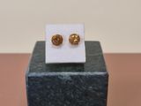 gold plated stud earrings on a marble stand on a pink surface
