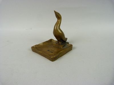 sculpture en bronze représentant un oiseau, posée sur un socle en bois, sur une surface blanche