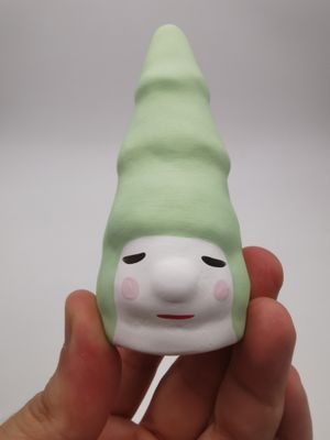 une main tenant une petite poupée coiffée d'un chapeau vert