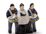three figurines of people playing drums on a white surface